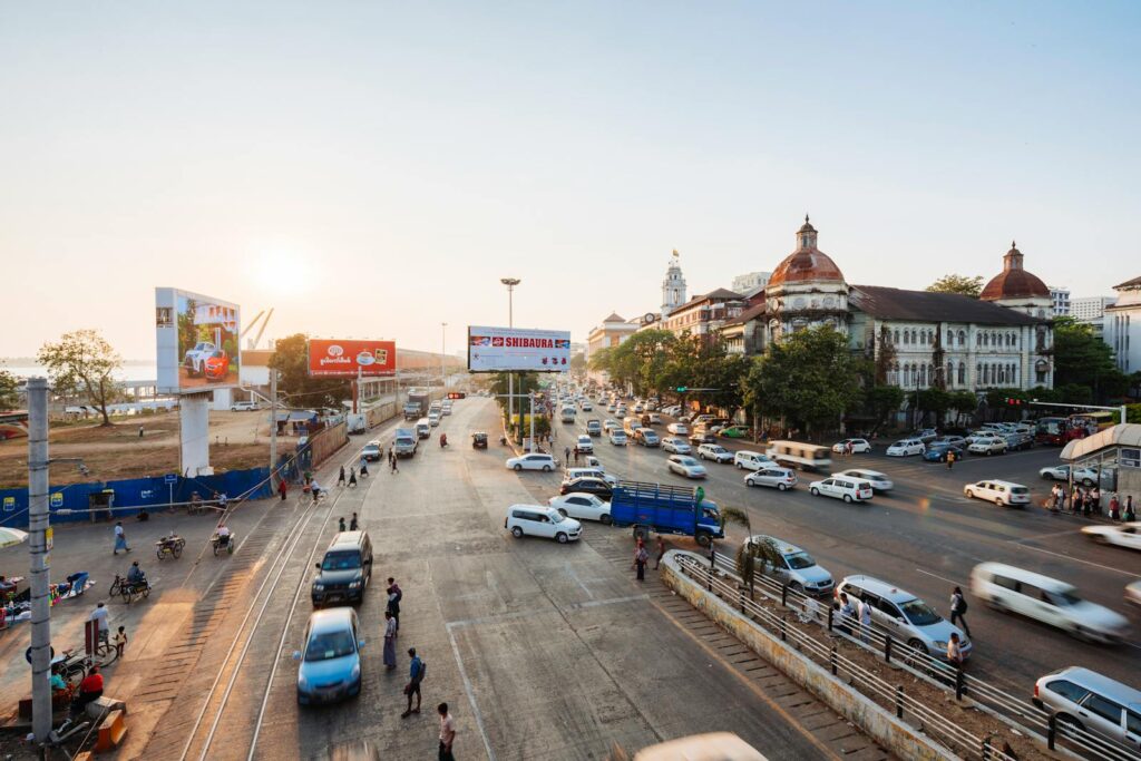A vibrant urban intersection in Yangon, Myanmar, at sunset with vehicles and pedestrians.