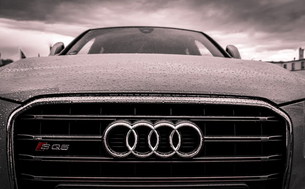 Close-up of a rain-covered Audi car grille showcasing luxury and elegance under cloudy skies.
