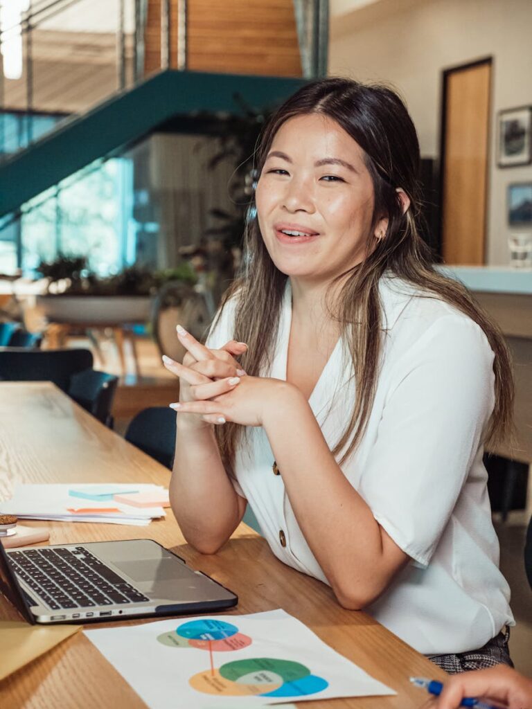 The Best CRM Software for Small Business: A Comprehensive Overview 14 A woman smiling at a workspace, sitting with a laptop and colorful charts.
