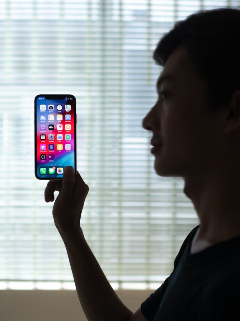 Profile of a man holding a smartphone with colorful apps, backlit indoors.