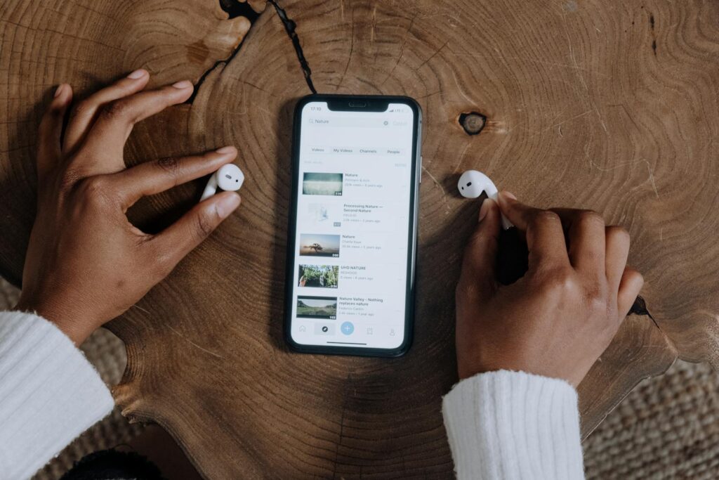 The Complete Social Media Audit Guide for Small Businesses 17 Hands interacting with smartphone and earbuds on a rustic wooden table, highlighting modern technology.