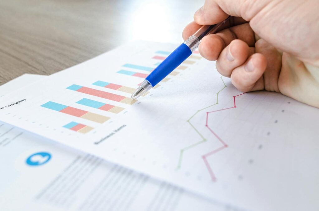 Why Keyword Research Services Are Essential for SEO Success 12 A close-up of a hand with a pen analyzing data on colorful bar and line charts on paper.