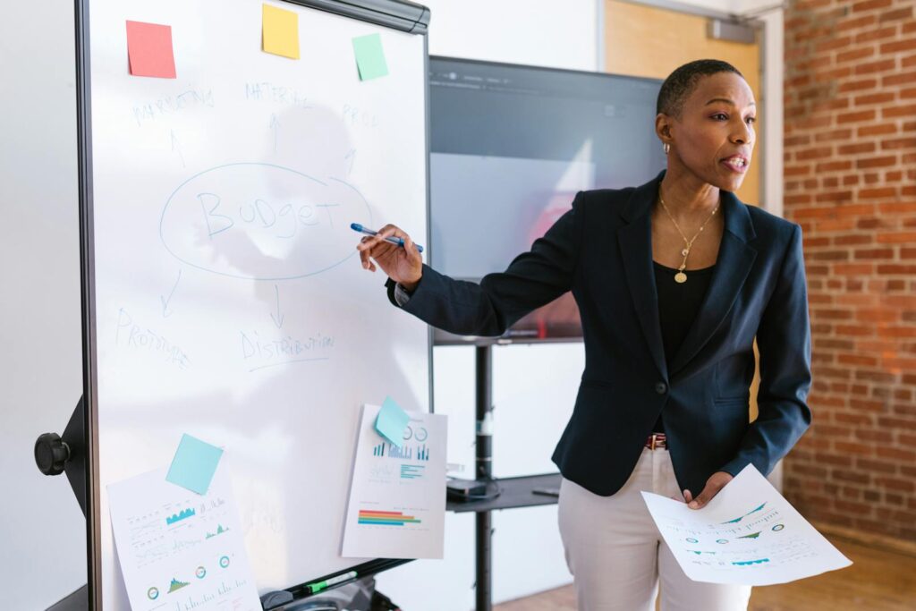 What Does a Social Media Manager Do—and Why Your Business Needs One 8 Professional businesswoman explaining budget strategy on a whiteboard during a meeting.