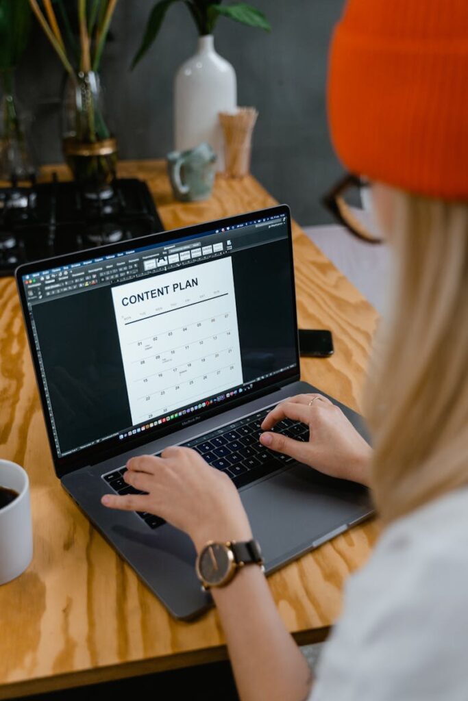Social Media Content Calendar Template: Save Time, Stay Consistent, Get Results 9 A woman working on a content plan using a laptop at a wooden table, showcasing productivity and planning.
