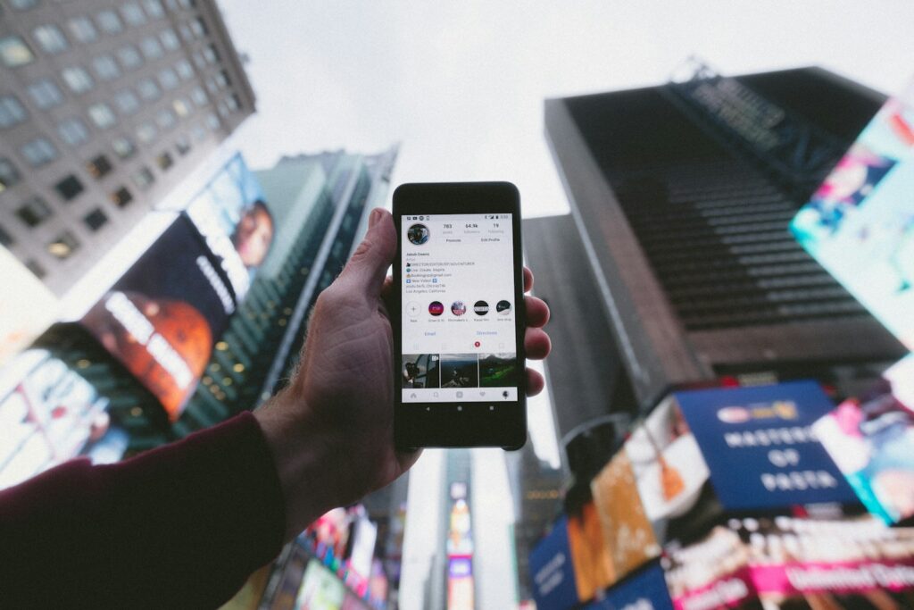 Social Media Presence: How to Elevate Your Business in 10 Simple Steps 12 high angle photo of person holding turned on smartphone with tall buildings background