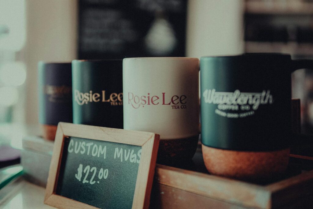 Close-up of custom coffee mugs in a cafe with a price sign, highlighting product details.